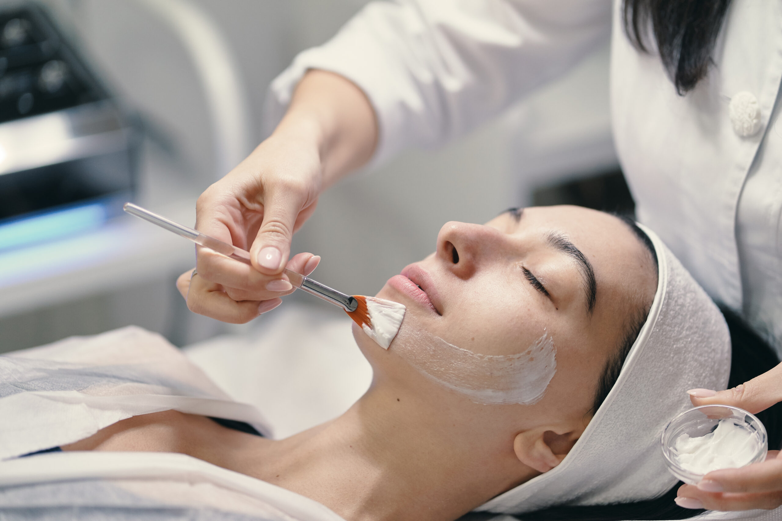 People, beauty, spa, cosmetology and skin care concept - Cosmetologist applying cream on a woman beautiful face with a cosmetologist brush.
